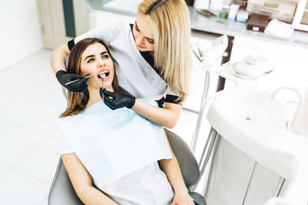 Pretty young female dentist making examination and treatment for young female patient in dental clinicの写真素材