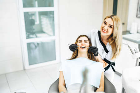 Pretty young female dentist making examination and treatment for young female patient in dental clinicの写真素材