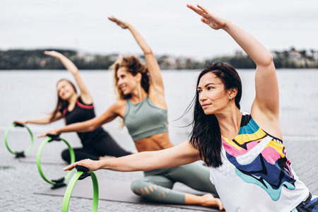 A group of sporty women doing stretching exercises with a special sports circle on the street near...