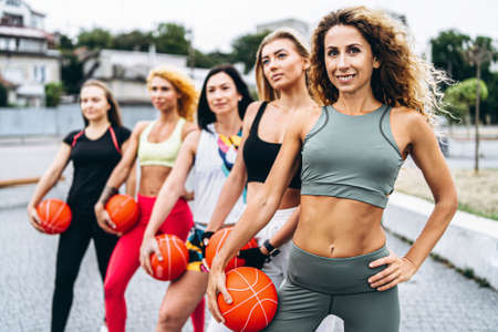A group of sporty women are posing at camera, performing exercises with orange balls, on the street near the water. Active lifestyle.の写真素材