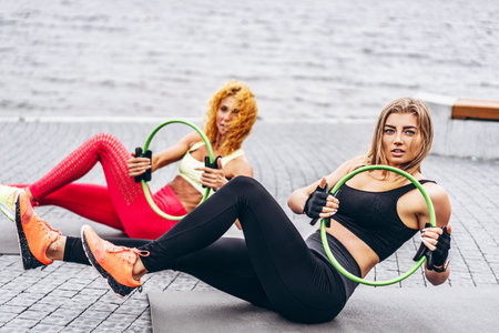 Two women practice yoga exercises on a mat on the street near the water. Active lifestyle. Yoga...
