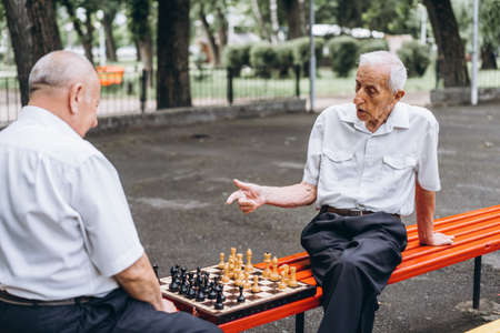 Two senior adult men playing chess on the bench outdoors in the parkの写真素材