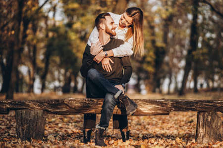 A young loving couple sitting on a wooden bench in the forest. Man and woman hugging and smiling on the background of autumn trees.の写真素材