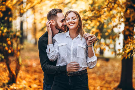 A young couple in love walking in the autumn park on a sunny day. The man gently hugs the woman. Love story.の写真素材