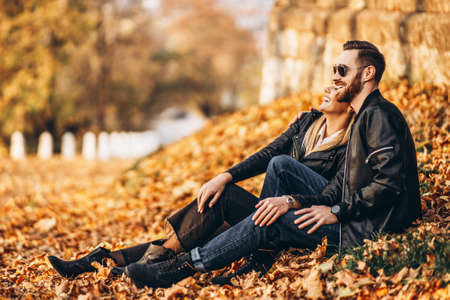 Portrait of a young loving couple, sitting in autumn leaf and enjoying nature. Love story.の写真素材
