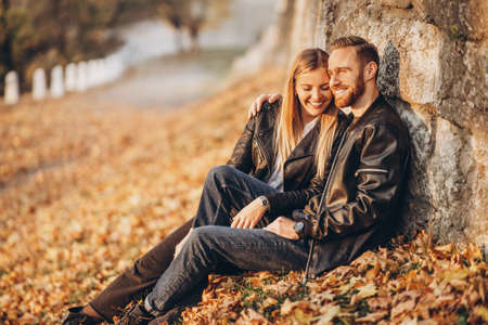 Portrait of a young loving couple, sitting in autumn leaf near stone wall and enjoying nature. Love story.の写真素材