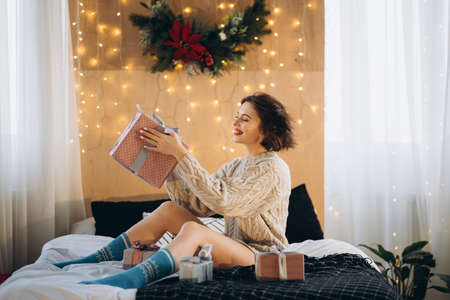 Happy and pretty brunette on the bed with gift boxes around her. New Year, Christmas, birthday, Valentineâs Day conceptの写真素材