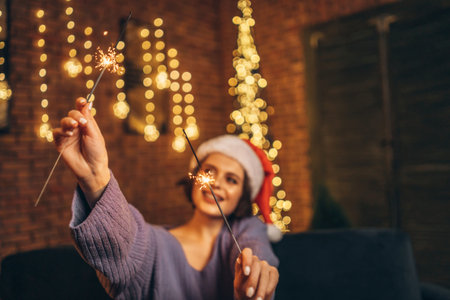 Pretty happy young brunette in christmas hat with sparkler in hands