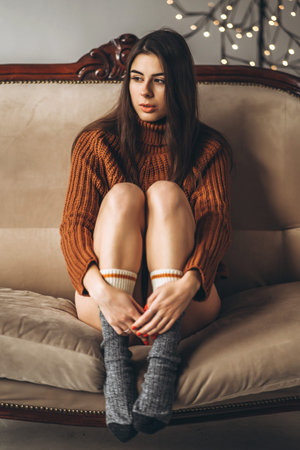 Pretty brunette girl in sweater and lingerie relaxing on the couch indoors
