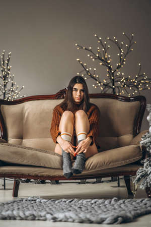 Pretty brunette girl in sweater and lingerie relaxing on the couch indoorsの写真素材