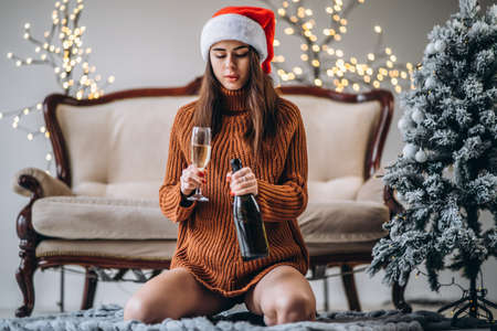 Christmas, New Year. Pretty girl in sweater and Christmas hat with champagne indoorsの写真素材