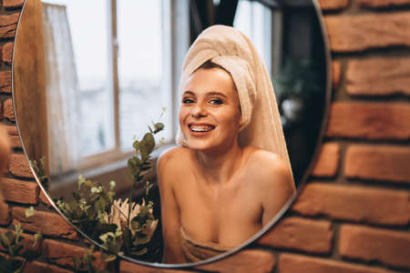 Pretty brunette with towel on her had standing near mirror in the bathroom after showerの写真素材