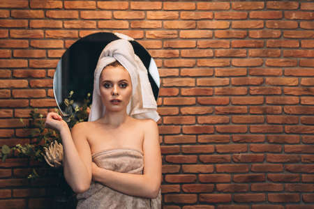 Pretty brunette with towel on her had standing near mirror in the bathroom after showerの写真素材