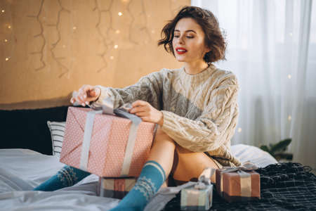Happy and pretty brunette on the bed with gift boxes around her. New Year, Christmas, birthday, Valentineâs Day conceptの写真素材