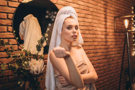 Pretty brunette with towel on her had standing near mirror in the bathroom after showerの写真素材