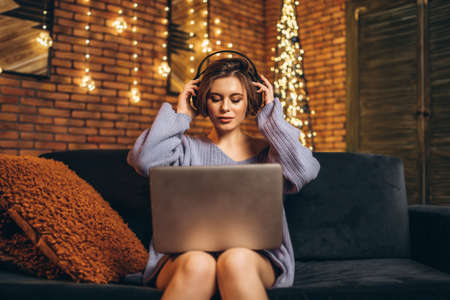 Pretty young brunette at home in headphones using laptop, online education, studying, shopping, working conceptの写真素材
