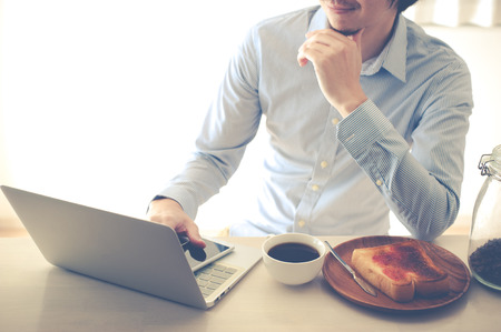 Japanese man who is operating a laptop while eating breakfastの写真素材