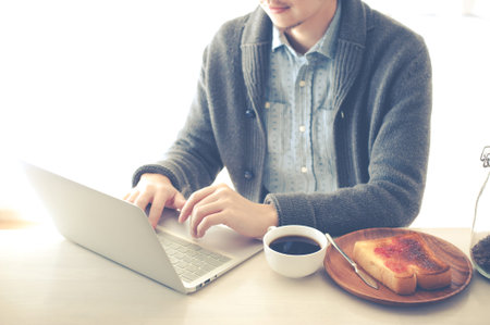 Japanese man who is operating a laptop while eating breakfast