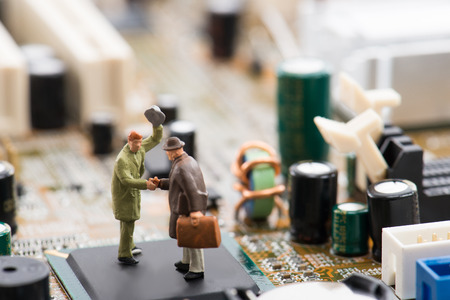 Miniature person are shaking hands on a computer motherboardの写真素材