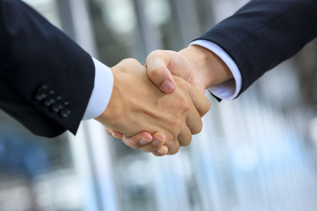 Shaking hands of businessmen and building backgroundの写真素材