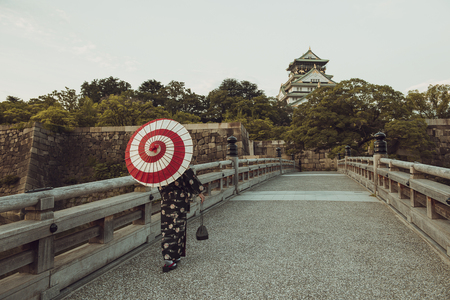 A Japanese woman in kimono and holding an umbrella walking towards a big traditional buildingの写真素材