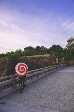 A Japanese woman in kimono and holding an umbrella walking towards a big traditional buildingの写真素材