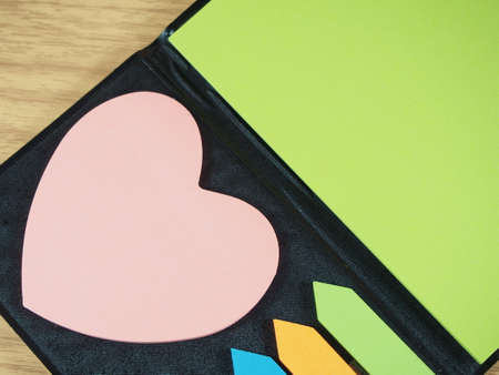 Sticky paper with pink heart shape, arrow shape on black notebook wood backgroundの写真素材