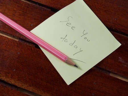 See you today, writing on yellow sticker paper and pink pencil on wood backgroundの写真素材