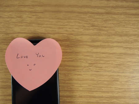 Love you with smiling face writing on sticker note and black mobile phone on wood backgroundの写真素材