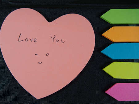 Love you with smiling face, drawing and writing on pose its paper with colorful heart and arrow on black  leatherette backgroundの写真素材