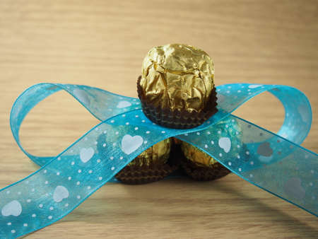 Pile of chocolate balls with covered golden aluminium foil, decorated blue sky ribbonの写真素材