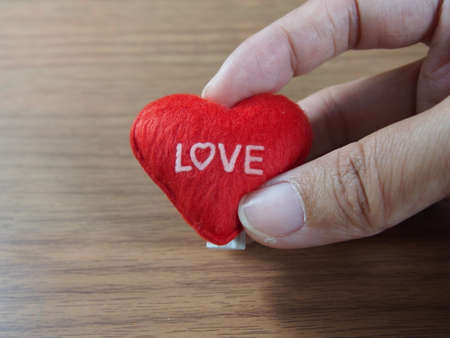 Holding little pillow with red heart shape and love word on wood backgroundの写真素材