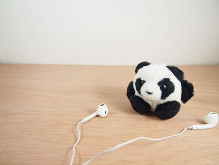 Round fat panda with white earphones on wooden backgroundの写真素材
