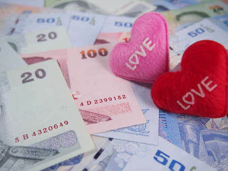 Love word on little heart pillows with pile of banknotes, saving and earning money conceptの写真素材
