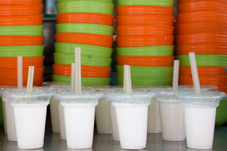 White cups of yoghurt in front of orange an green bowlsの写真素材
