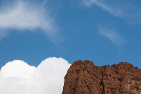 White clouds next to a mountain with the same shape as the mountain and blue skyの写真素材