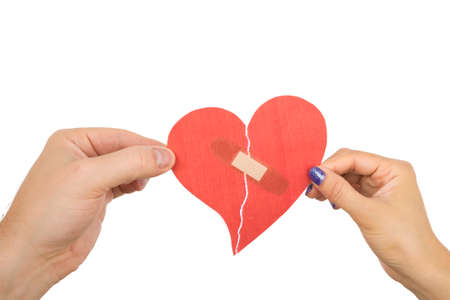 Male and female hand holding a red paper heart taped with bandagesの写真素材