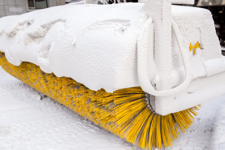 Snow remover vehicle with yellow brush covered in ice and snow