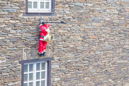 Santa climbing up to a white window on an old wallの写真素材
