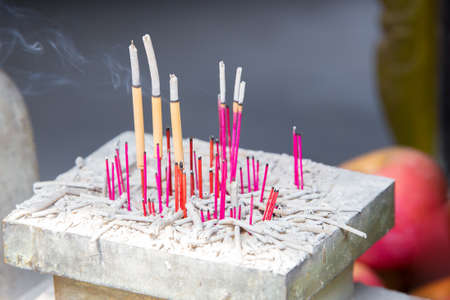 Different colored incentive sticks burning down on a small altar with a fruit background in a Chinese templeの写真素材