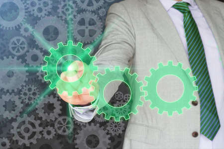 Businessman in a grey suit and a green tie pressing one of three gears on a gear backgroundの写真素材