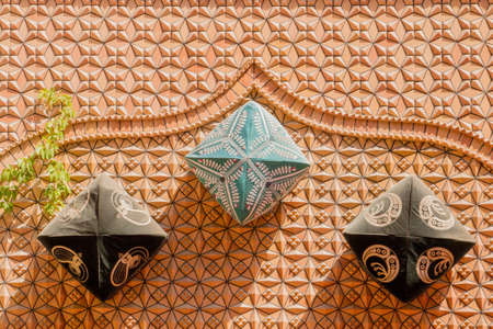 Xinjiang,China 09/05/2015 Three traditional Chinese dopa hats attached to an orange wall with decorations throwing a shadow on a sunny dayのeditorial素材