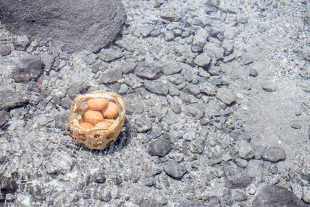 Basket with brown eggs boiling in the water of a hot spring in a park in thailand