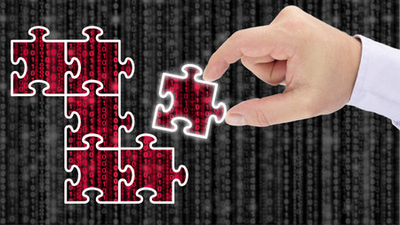 Hand putting together a puzzle reveiling red datastreams on top of a blurry grey digital matrix...