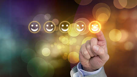 Hand pressing yellow smiley button of performance rating on a colored background with bokehの写真素材