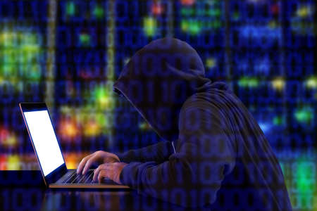 Hacker in a green hoody sitting in front of a notebook with colored server background and binary streams cybersecurity conceptの写真素材