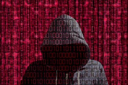 Hacker in a grey hoody standing in front of a red datastream background of binary streams...