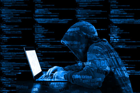Hacker in a blue hoody standing in front of a code background with binary streams and information security terms cybersecurity conceptの写真素材
