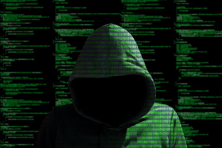 Hacker in a green hoody standing in front of a code background with binary streams and information...