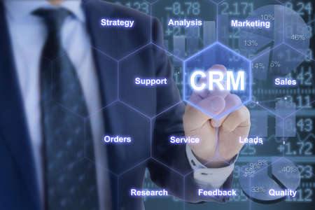 Businessman in a blue suit touching a crm tile in a hexagon grid with keywords customer relationship management conceptの写真素材